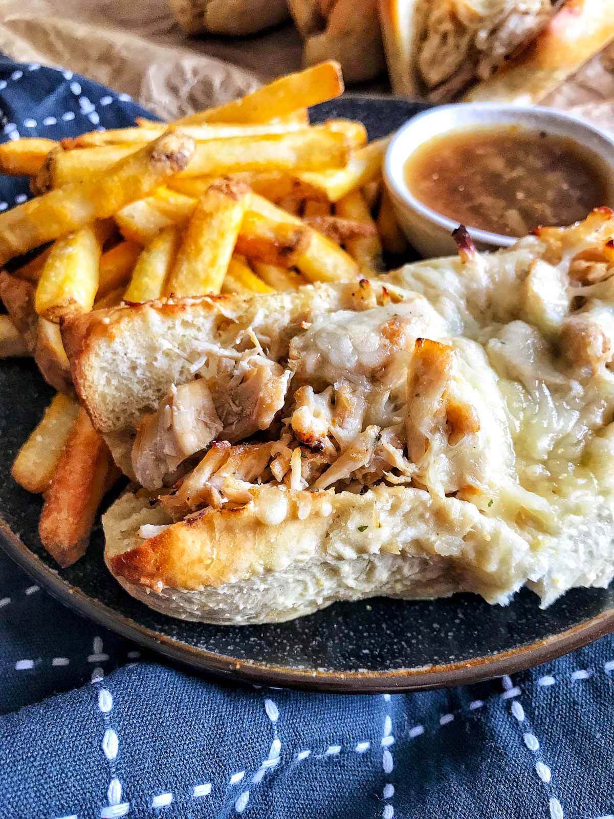 french onion chicken dip sandwich with a side of fries and small bowl of au jus.
