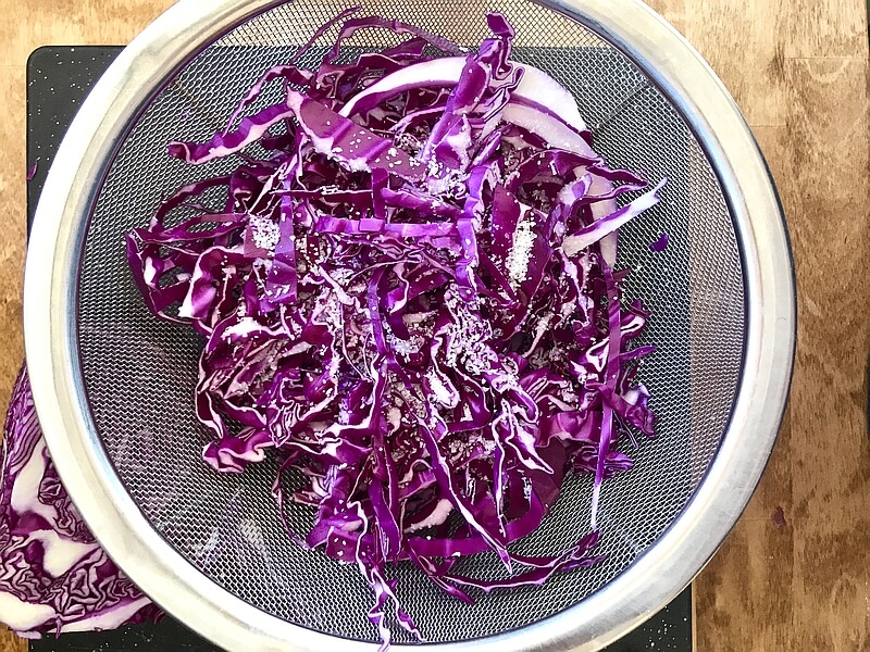 Strips of the red cabbage piled lightly together in a strainer, kosher salt grains dusted over the top.