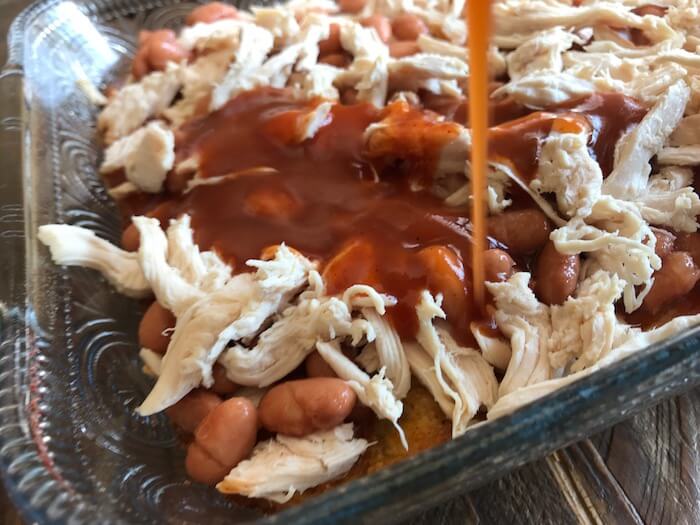 Enchilada sauce being poured over pinto beans and chicken breast