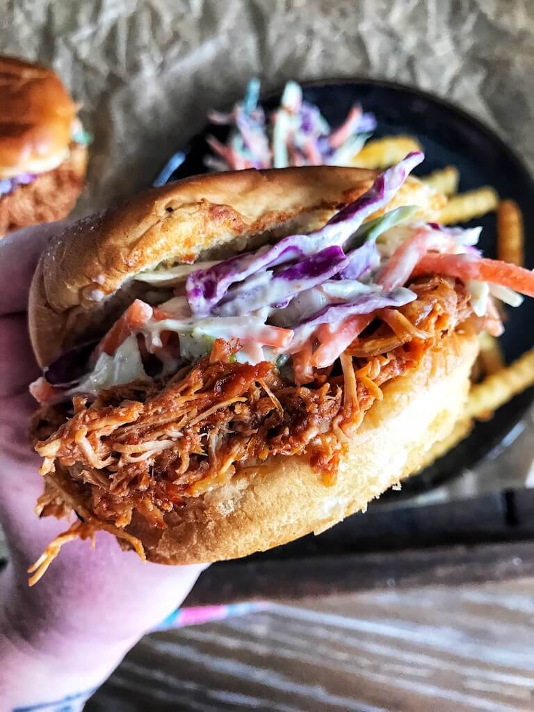 Crockpot Pulled BBQ Chicken being held above a plate of coleslaw and french fries