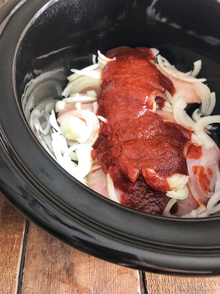 Chicken breasts, homemade BBQ sauce, and sliced onions in the crockpot before cooking
