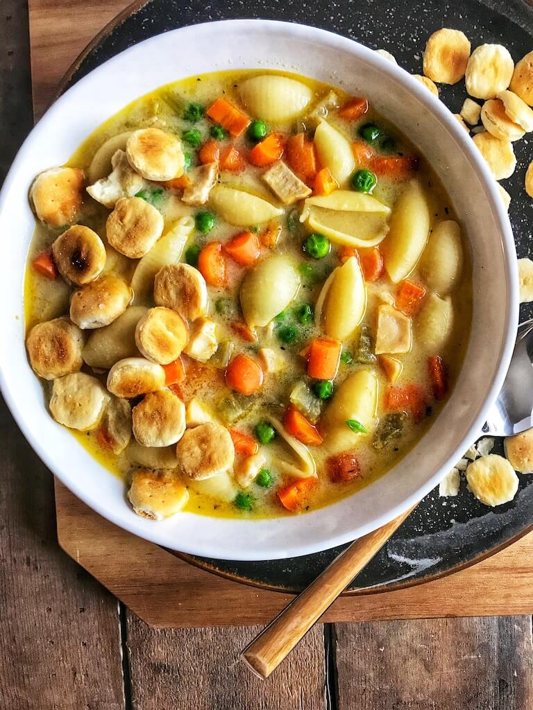 bowl of creamy chicken noodle soup with crackers on a plate with a spoon