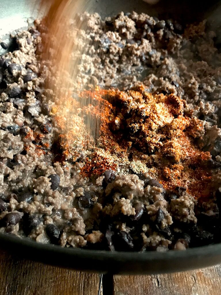 seasoning being sprinkled over the beef and beans 
