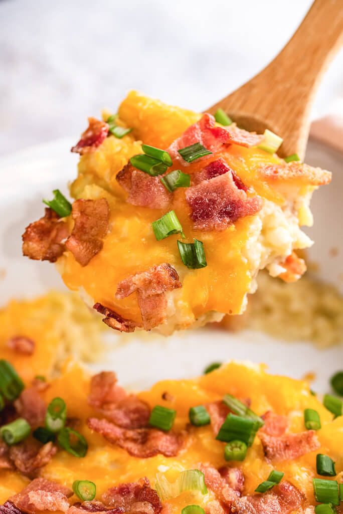 loaded cauliflower and potato casserole with bacon, cheese, and green onion being scooped out of a casserole dish