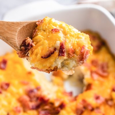 cauliflower and potato casserole with cheese and bacon being scooped out of the pan