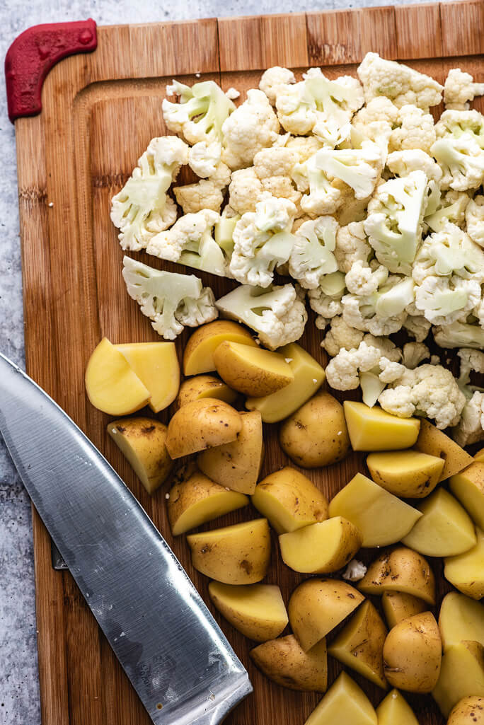 knife, potato chunks, cauliflower chunks on a cutting board
