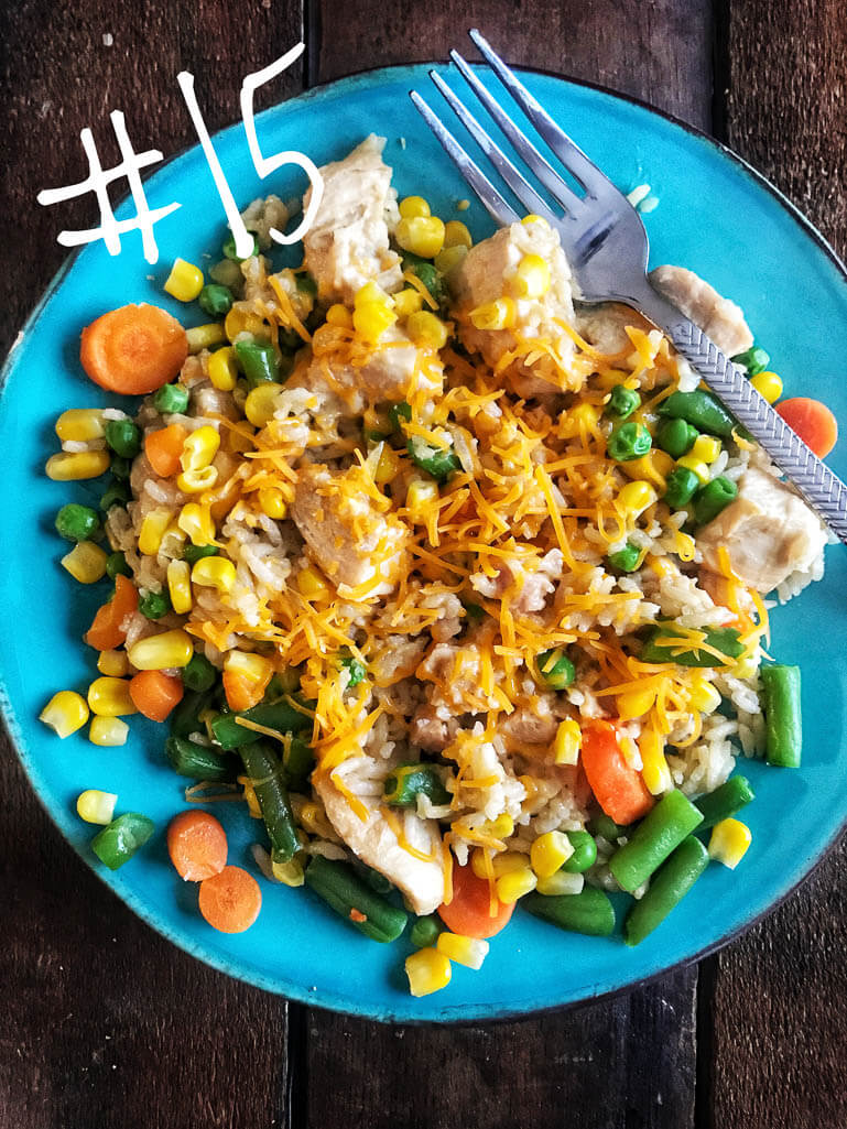 chicken and rice with cheese and corn, carrots, green beans on a bright blue plate with a fork