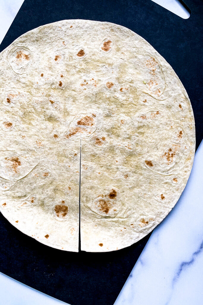 large tortilla, cut in the middle, on a black cutting board