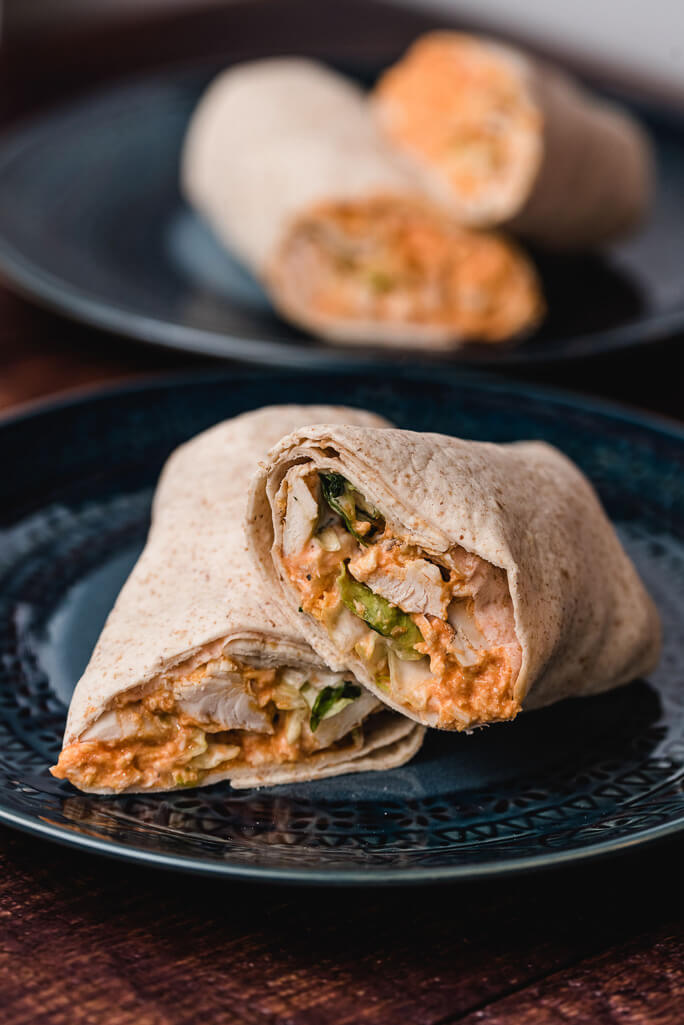 buffalo chicken and lettuce inside a wrap on a dark blue plate with the same out of focus in the background