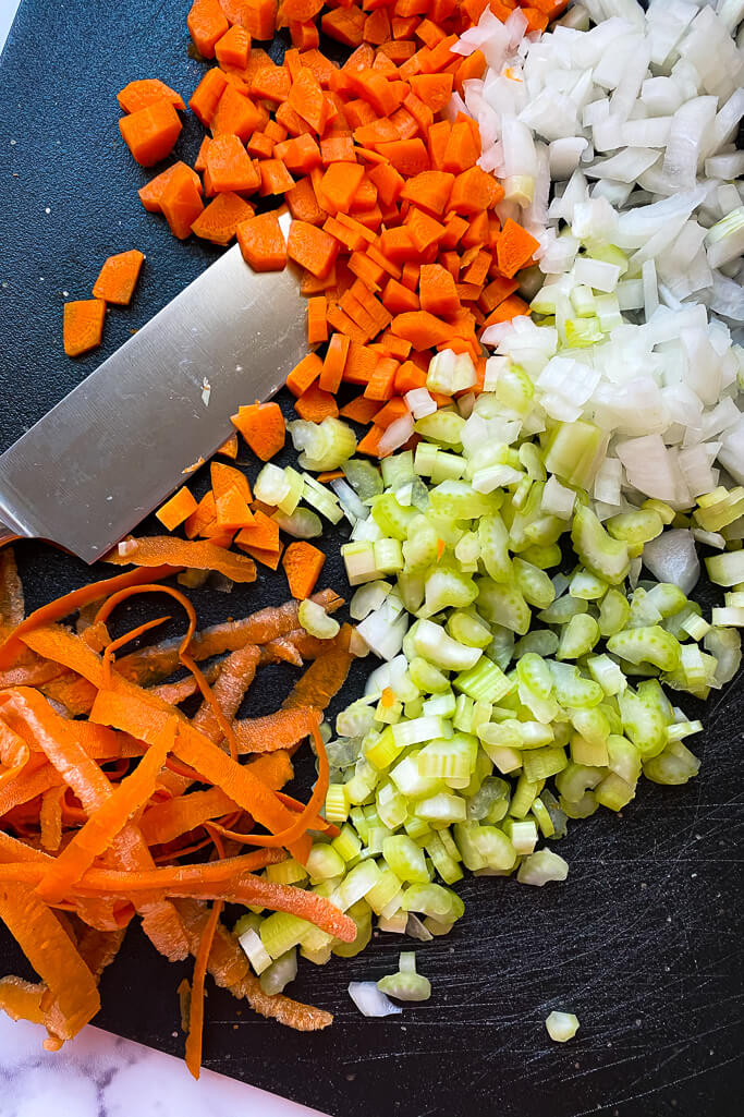 chopped onions, celery, and carrots on a black cutting board with a knife 