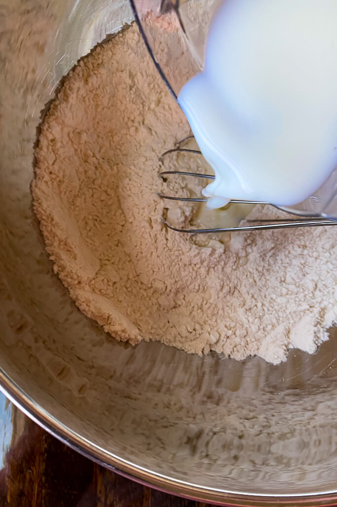 bowl with flour, whisk, and milk being poured into the bowl 