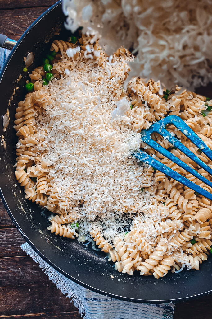 grated Parmesan being added to cooked rotini and peas