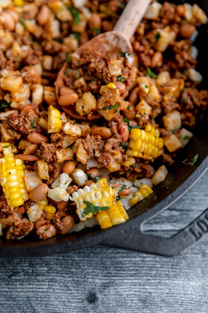 lodge skillet filled with corn, ground beef, pinto beans, cilantro, and potatoes