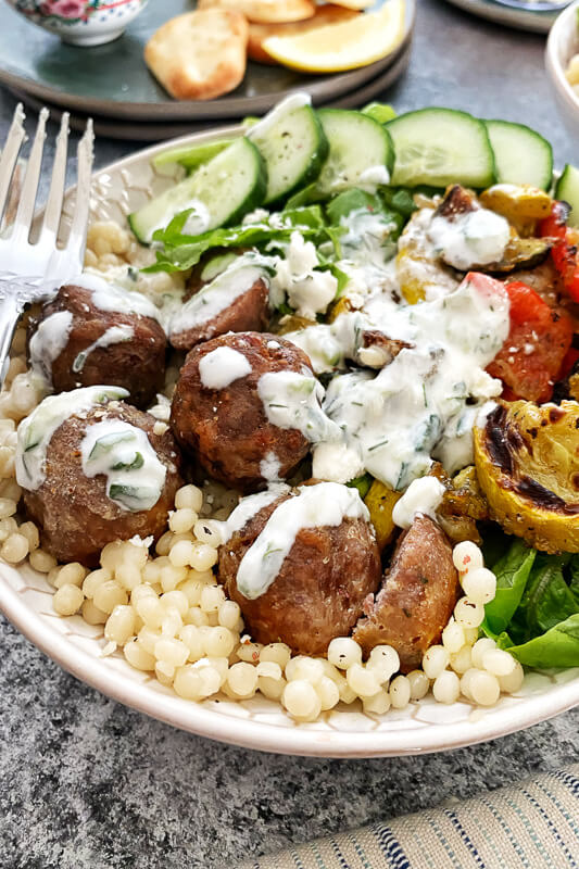 meatballs with tzatziki sauce on a bed of couscous and a fork and cucumber in the background