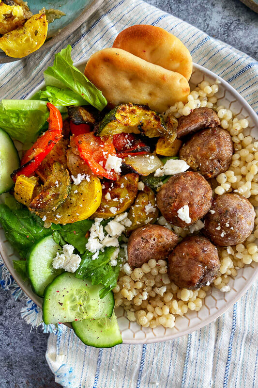 bowl with couscous cucmbers, tomatoe, lettuce, and greek meatballs