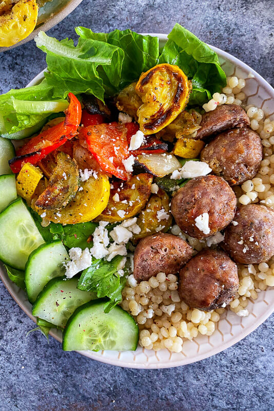 Greek Meatballs in a bowl with cucumbers, greens, and couscous