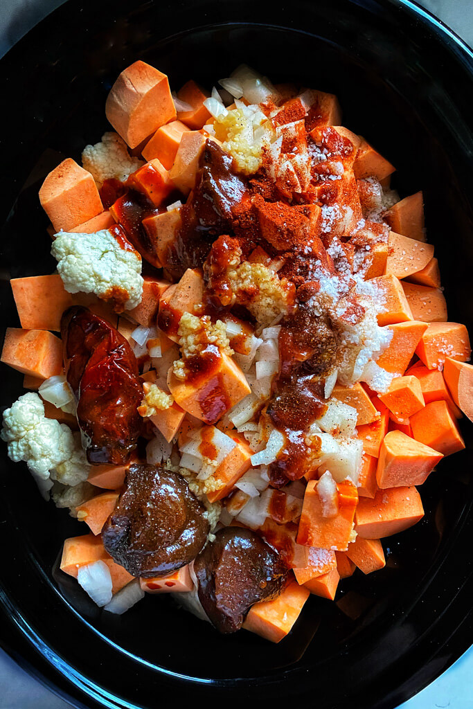 slow cooker loaded with sweet potatoes, cauilflower, adobo, and seasonings