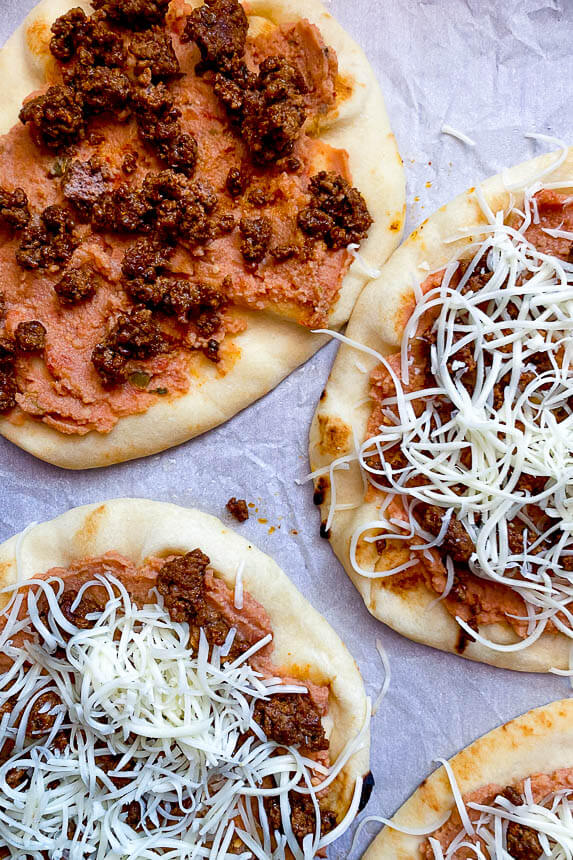 naan flatbreads with refried beans, taco meat, and shredded mozzarella 