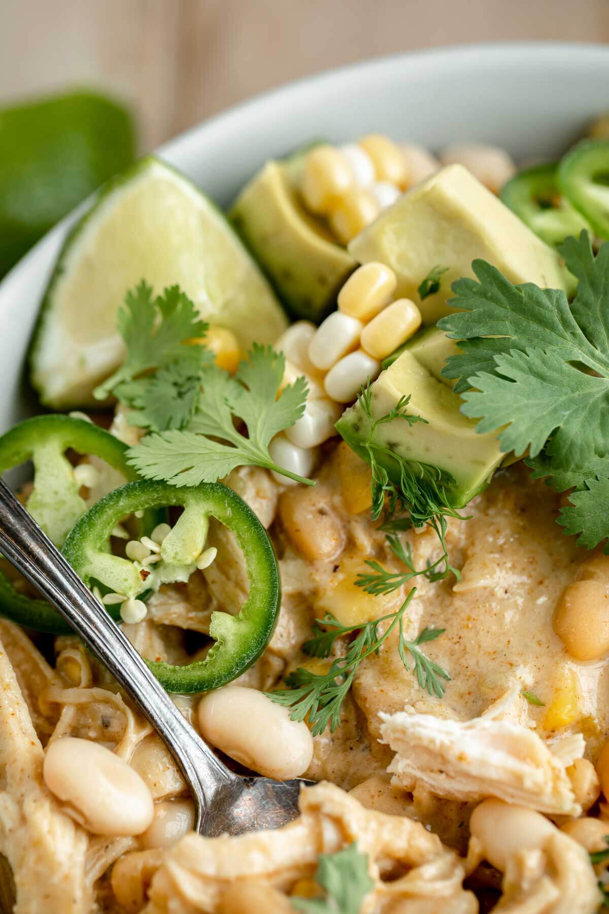instant pot white chicken chili in a bowl with toppings: lime, cilantro, avocado, jalapeno