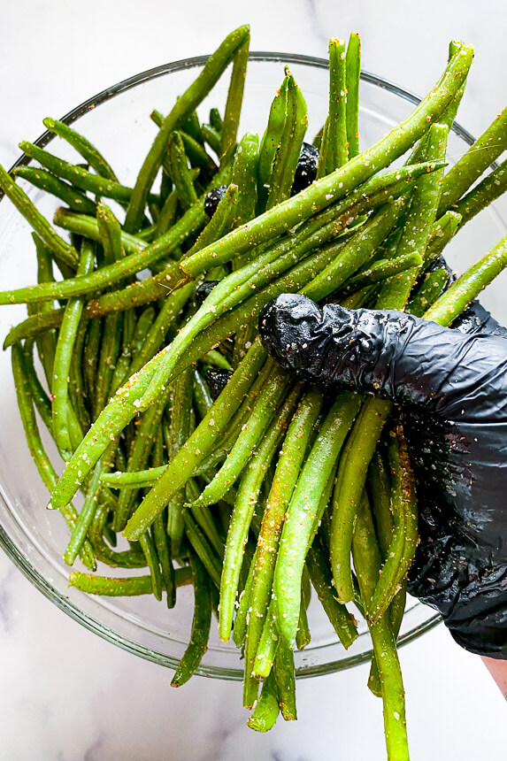 raw green beans in bowl with seasonings being rubbed into them