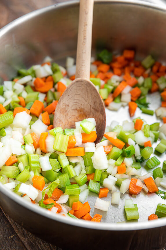 carrots, onions, and celery being stirred in a pan