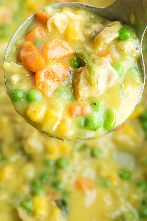 Ladle of creamy chicken pot pie soup filled with chicken, carrots, peas, and corn over a pot of thick golden broth.