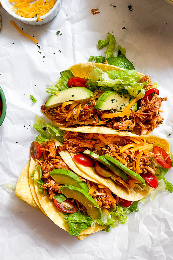 tacos filled with salsa chicken, lettuce, tomatoes, cheese, and slices of avocado