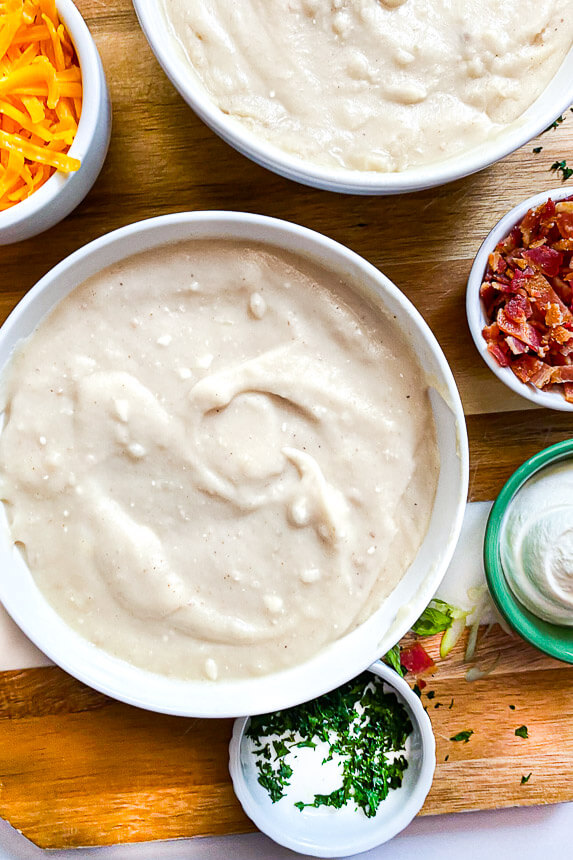 bowl of potato soup with small bowls of sour cream, crumbled bacon, and shredded cheese on the side