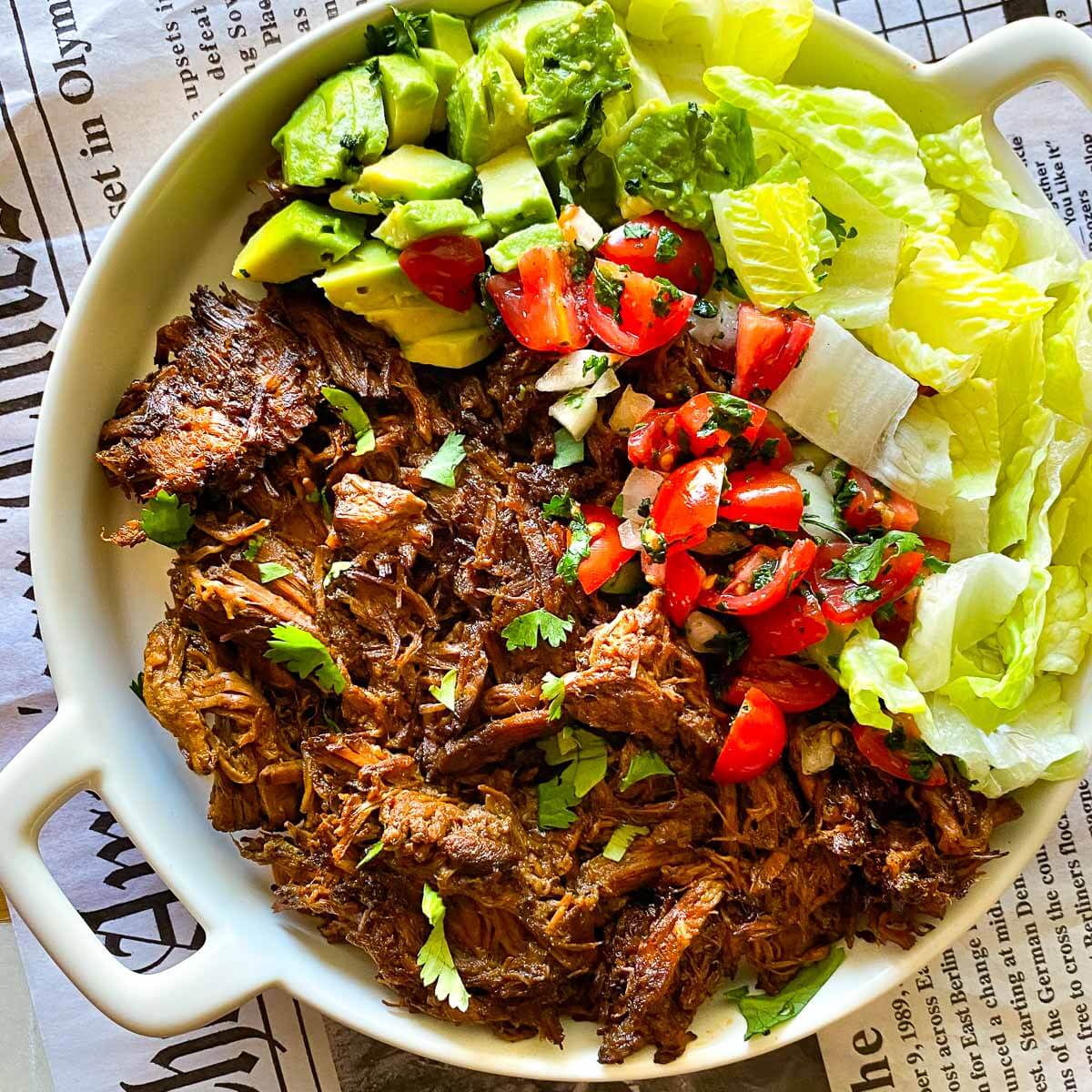 mexican shredded beef on plate with lettuce, tomatoes, and sliced avocado