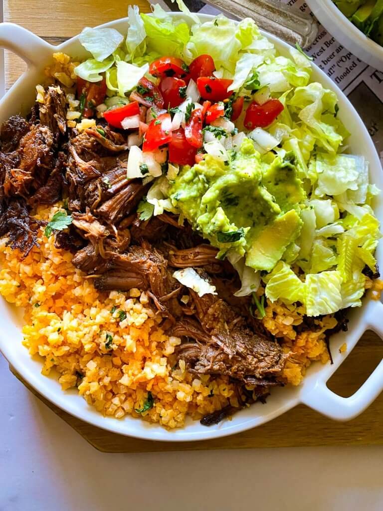 plate full of cauliflower Mexican Rice, shredded beef, lettuce, pico, and guacamole