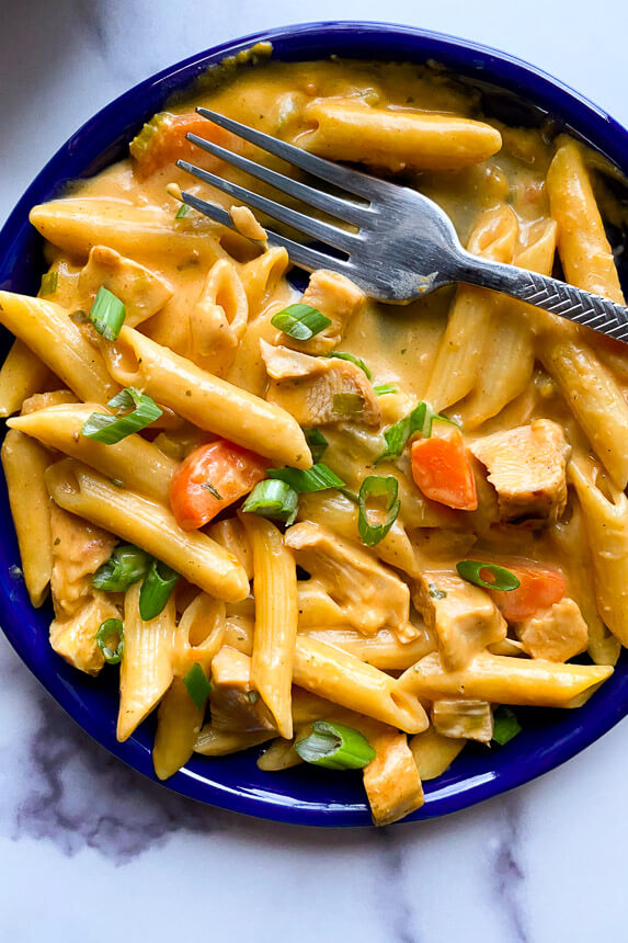 buffalo chicken pasta on plate with fork garnished with diced green onion