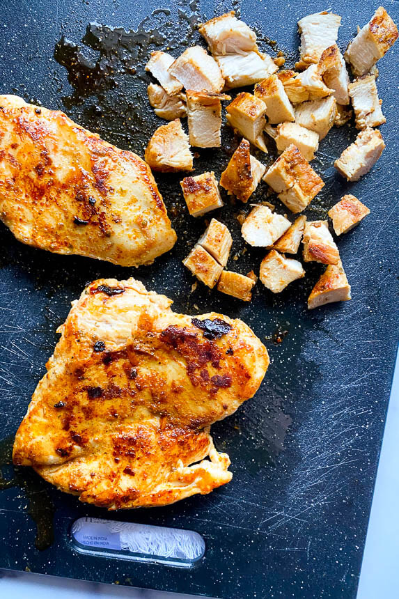 cooked chicken on cutting board being cut into small cubes