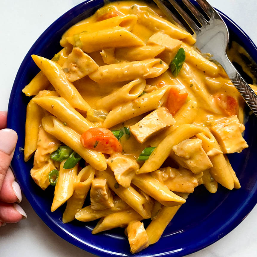 Hand holding blue plate with pile of buffalo chicken pasta and a fork on the side 