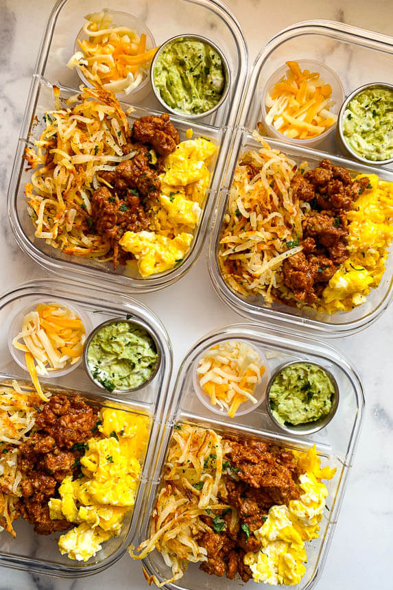 containers for meal prep loaded with hash browns, turkey meat, scrambled eggs, small cups of guacamole and shredded cheese