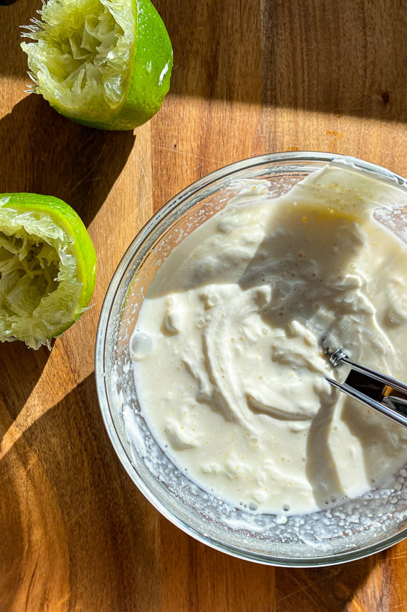 bowl of sour cream being stirred on a wooden cutting board with limes on the side