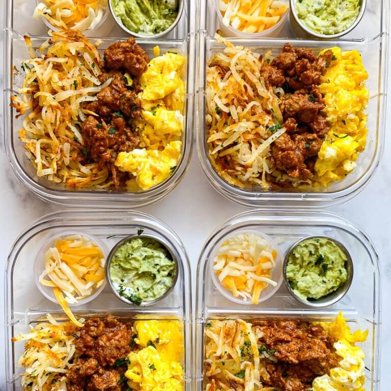 four meal prep containers full of scrambled eggs, taco meat, crispy shredded hash browns, small bowl of guacamole, small bowl of shredded cheese