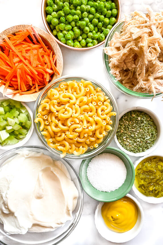 bowl of peas, bowl of shredded carrots, bowl of diced celery, bowl of macaroni, bowl of mayo, bowl of kosher salt, bowl of mustard, bowl of ranch seasoning mix, bowl of shredded and cooked chicken breast 