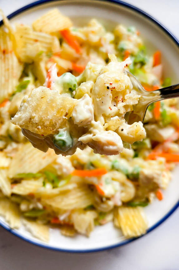 close up of macaroni noodles, diced chicken, and peas on a fork with a potato chip topping