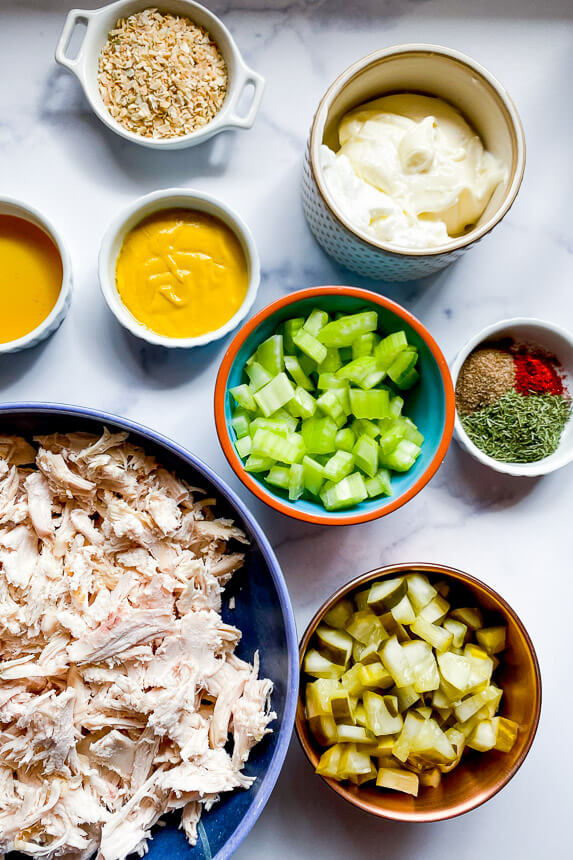 ingredients: bowl of shredded chicken breast, bowl of diced pickles, bowl of diced celery, bowl of yellow mustard, bowl of honey, bowl of dried minced onion, bowl of nonfat greek yogurt and mayo, bowls of spices: dill, smoked paprika, and celery salt