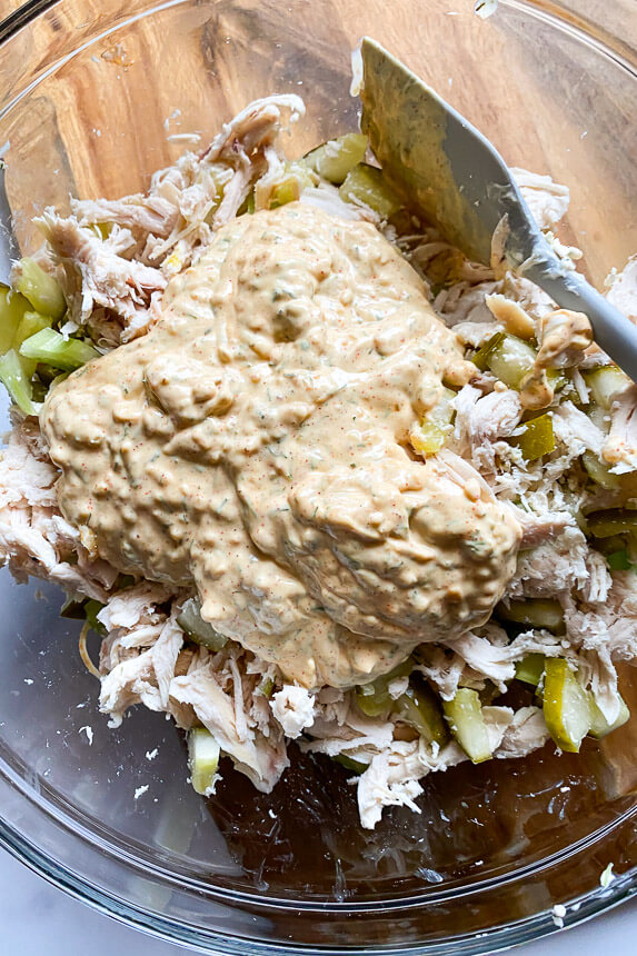 bowl with dressing on top of chicken, celery, and pickles