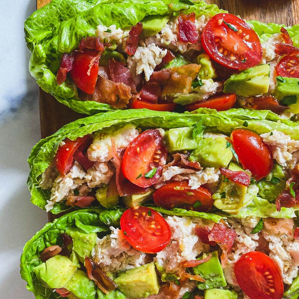 romaine lettuce leaves with chicken salad, bacon, tomato, and diced avocado stuffed inside 