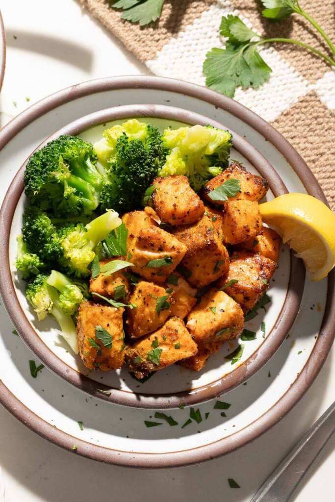 air fryer salmon on a plate served with broccoli and lemon wedge