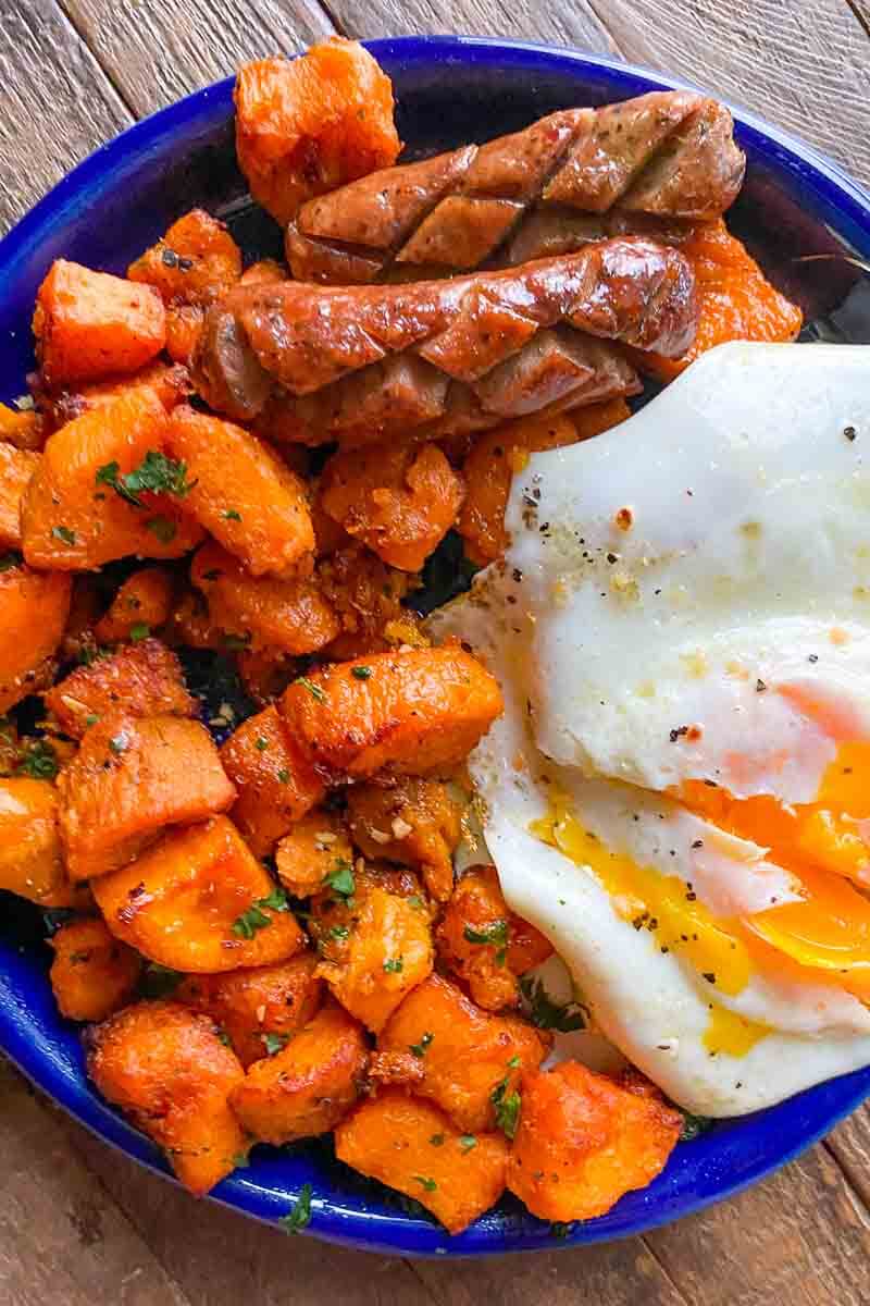 blue plate withe cubes of sweet potatoes, over easy egg with runny yolk, two peices of scored sausage