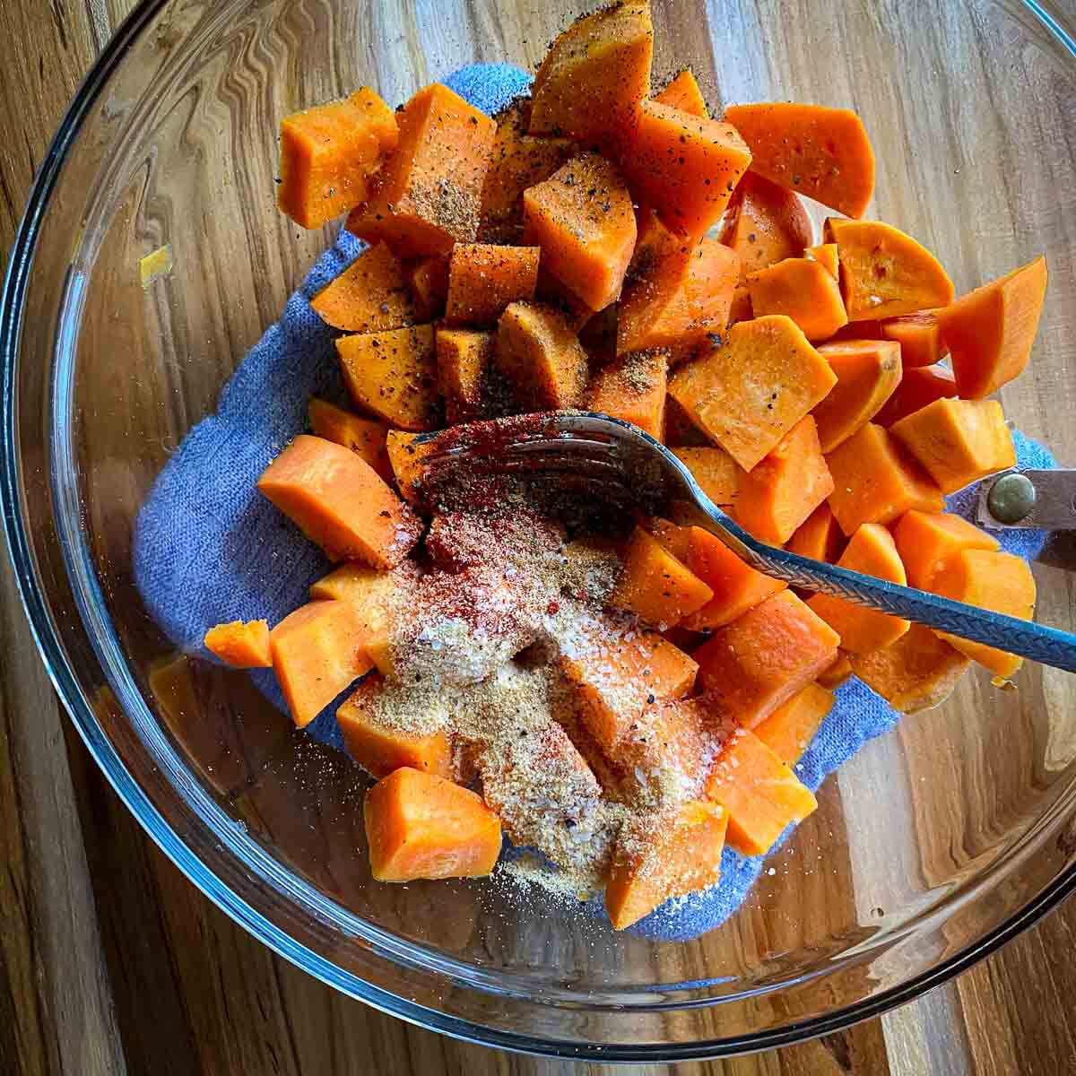 sweet potatoes in clear glass bowl with spices and fork 