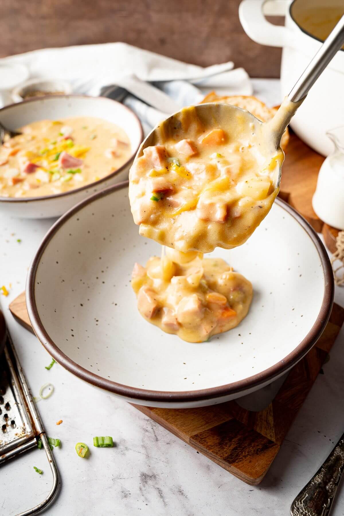 Close-up of a ladle pouring creamy ham and potato soup with diced ham, potatoes, and vegetables into a bowl, perfect for a cozy fall or winter dinner.