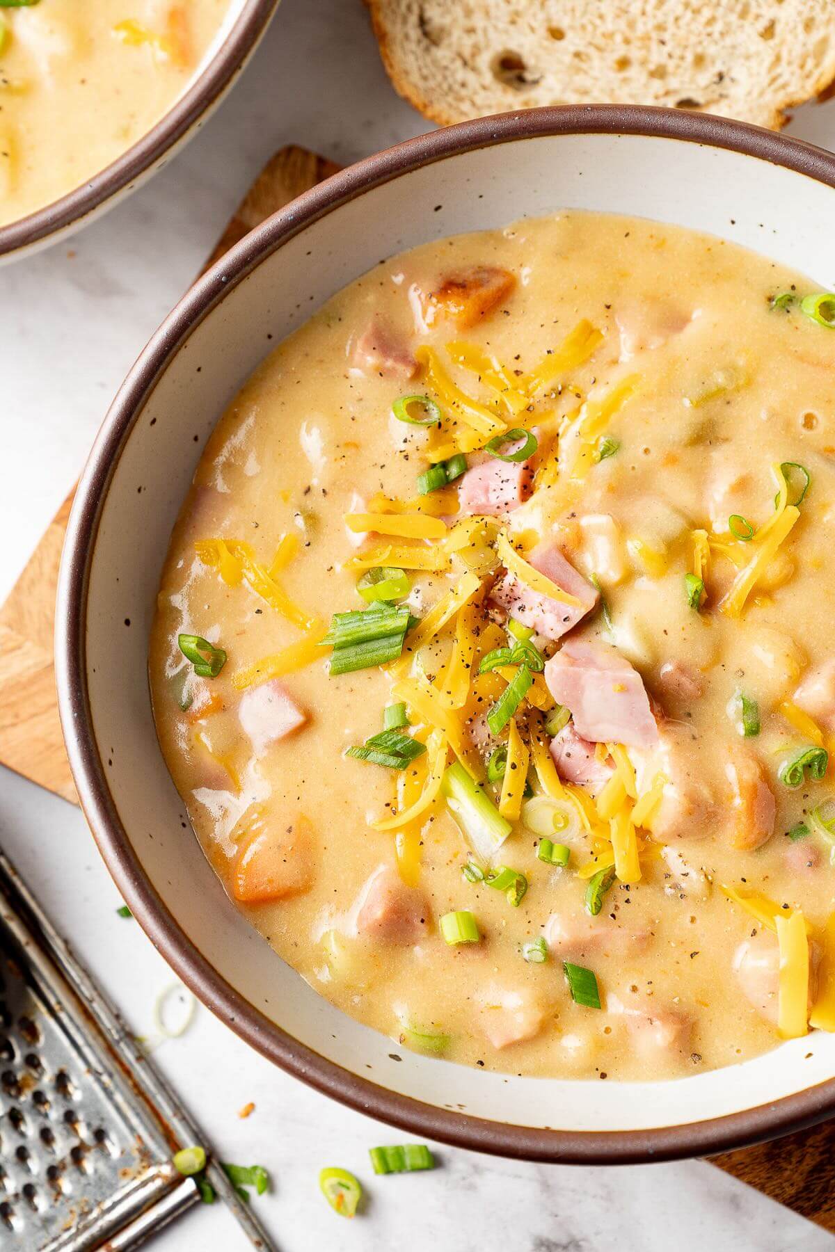 ham and potato soup in a white bowl topped with diced ham, green onion, and shredded cheddar cheese
