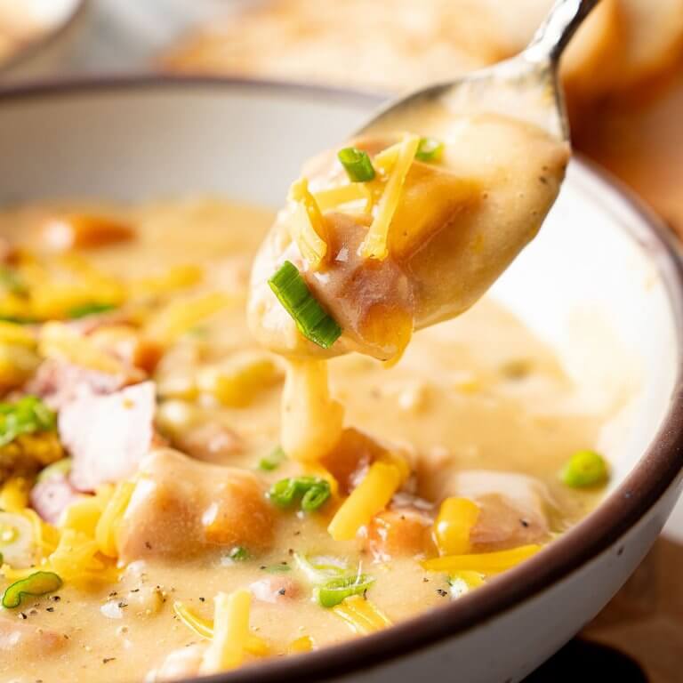 Creamy Ham and Potato Soup in a white bowl with a spoon lifting a thick, cheesy bite full of tender potatoes and diced ham.