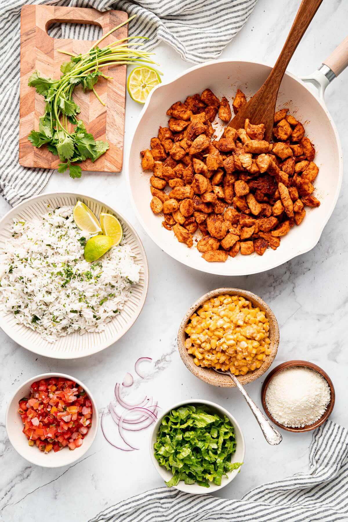 all the makings to assemble street corn chicken rice bowls: cilantro, chicken, rice, mexican street corn, pico de gallo, cotija, onions