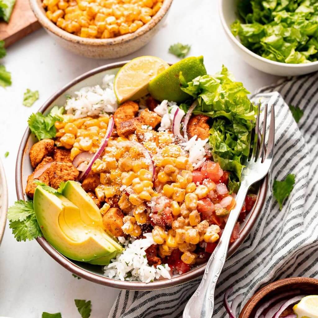 Street corn chicken rice bowl with charred corn, seasoned chicken, cilantro-lime rice, avocado, lettuce, and pico de gallo.