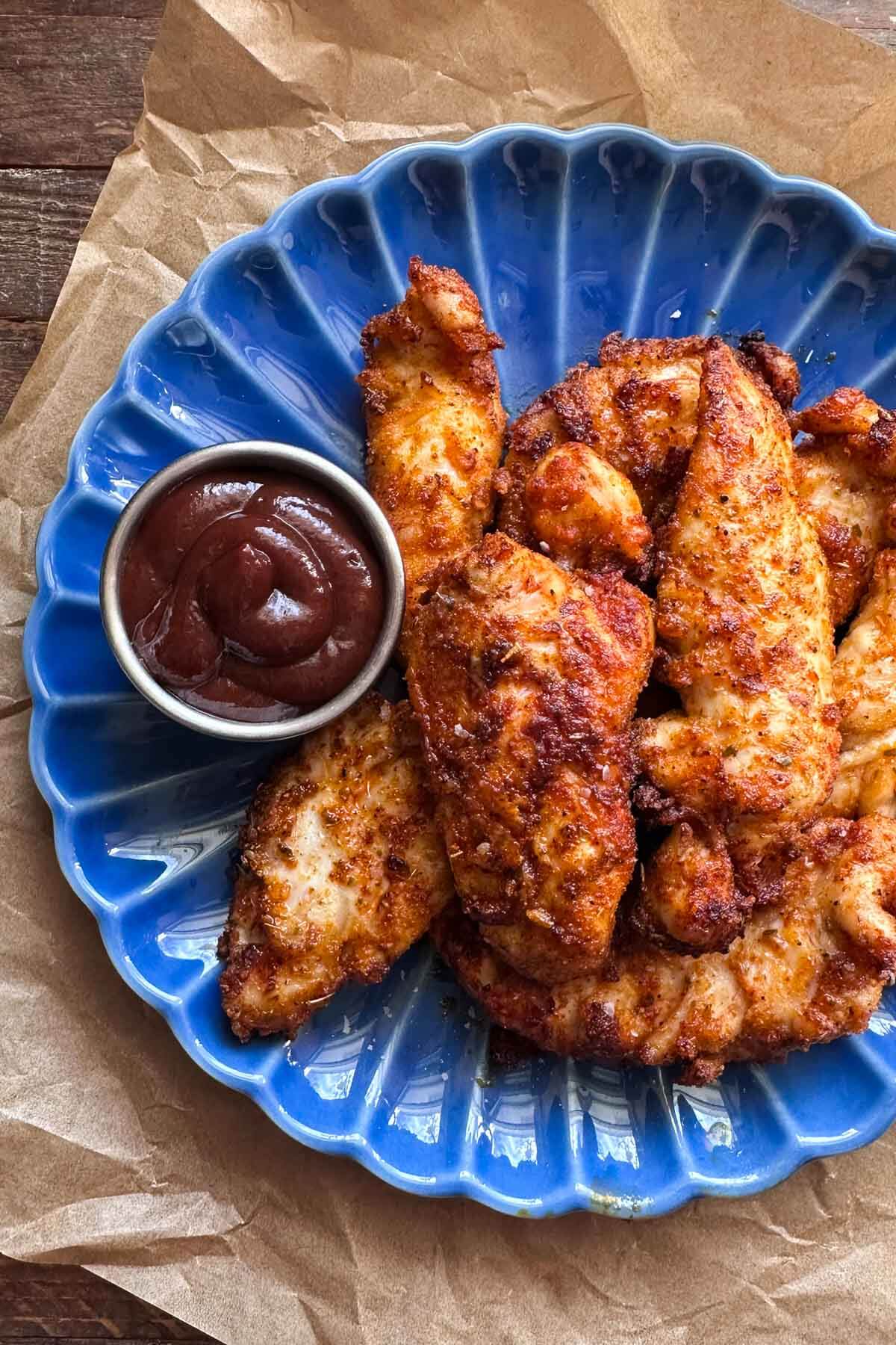 air fryer chicken tenderloins on a blue plate with a small dish of bbq sauce on the side